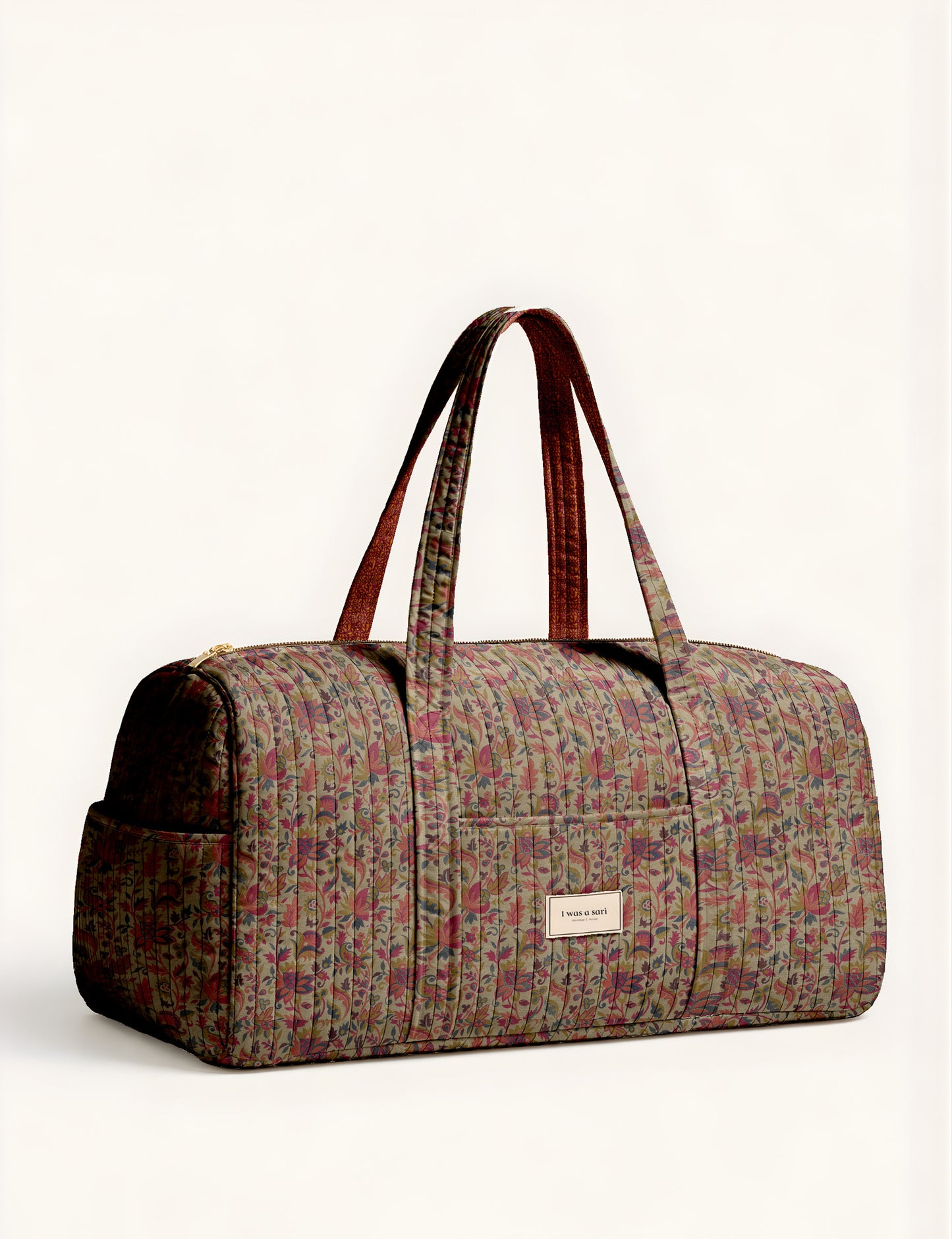 Quilted brown paisley barrel bag with double handles, front pocket, and gold zipper, shown in side angle view