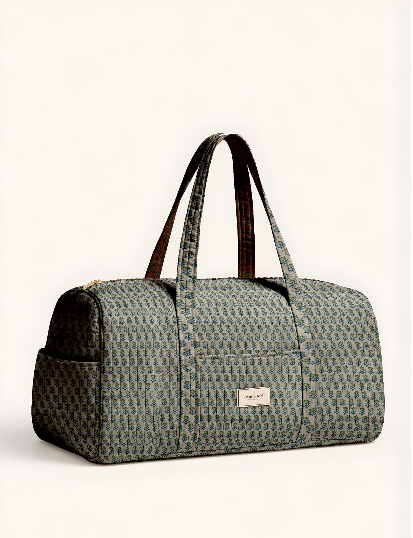 Quilted brown paisley barrel bag with double handles, front pocket, and gold zipper, shown in side angle view