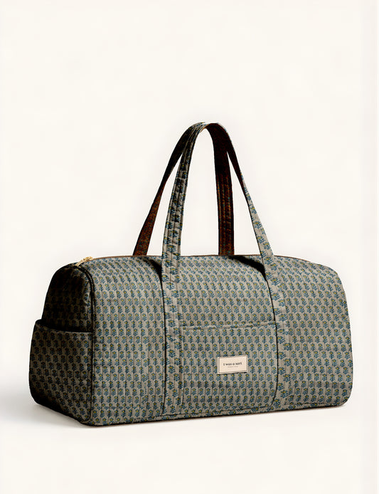 Quilted brown paisley barrel bag with double handles, front pocket, and gold zipper, shown in side angle view