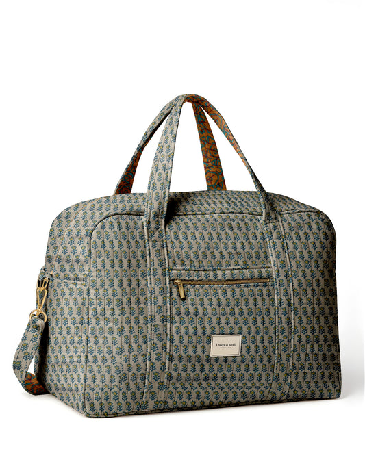 Brown quilted duffle bag with paisley pattern, front zip pocket, dual handles, and label reading "I was a sari"