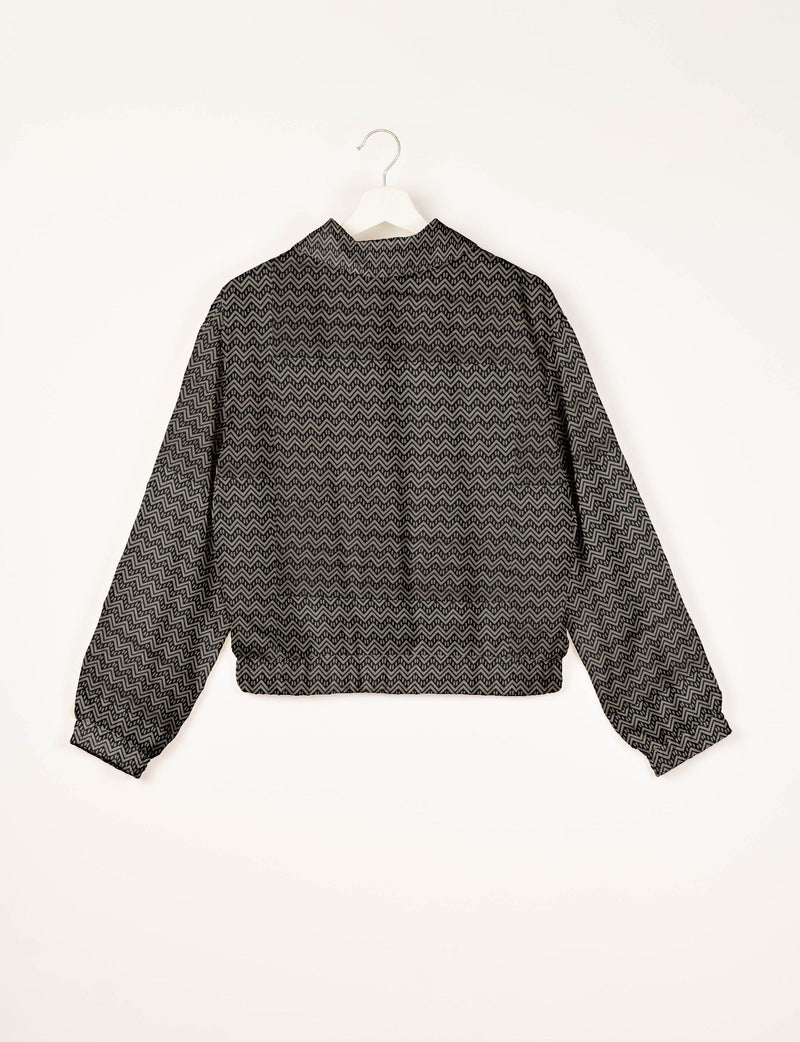 Beige bomber jacket with black geometric zigzag pattern, long sleeves, elastic cuffs and waistband, shown from back on