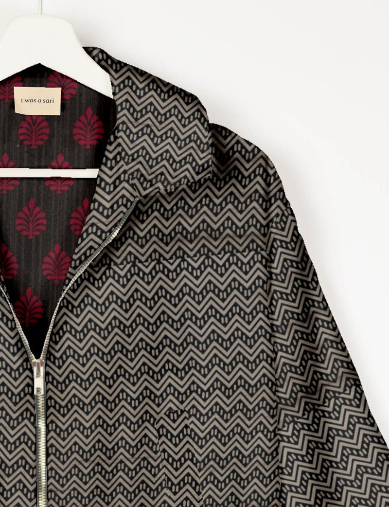 Beige and black geometric patterned bomber jacket with front zipper, hanging on white hanger, label reads "I was a sari"