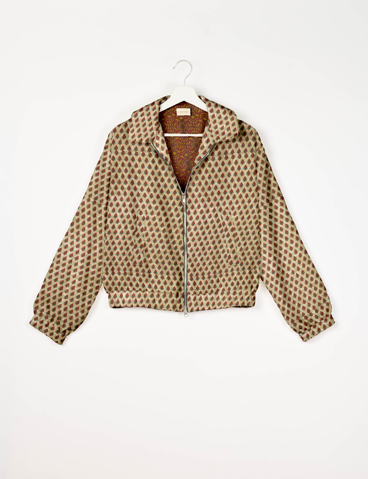 Beige bomber jacket with red and green Indian ethnic print, front zipper, collar, and elastic cuffs, hanging on white hanger