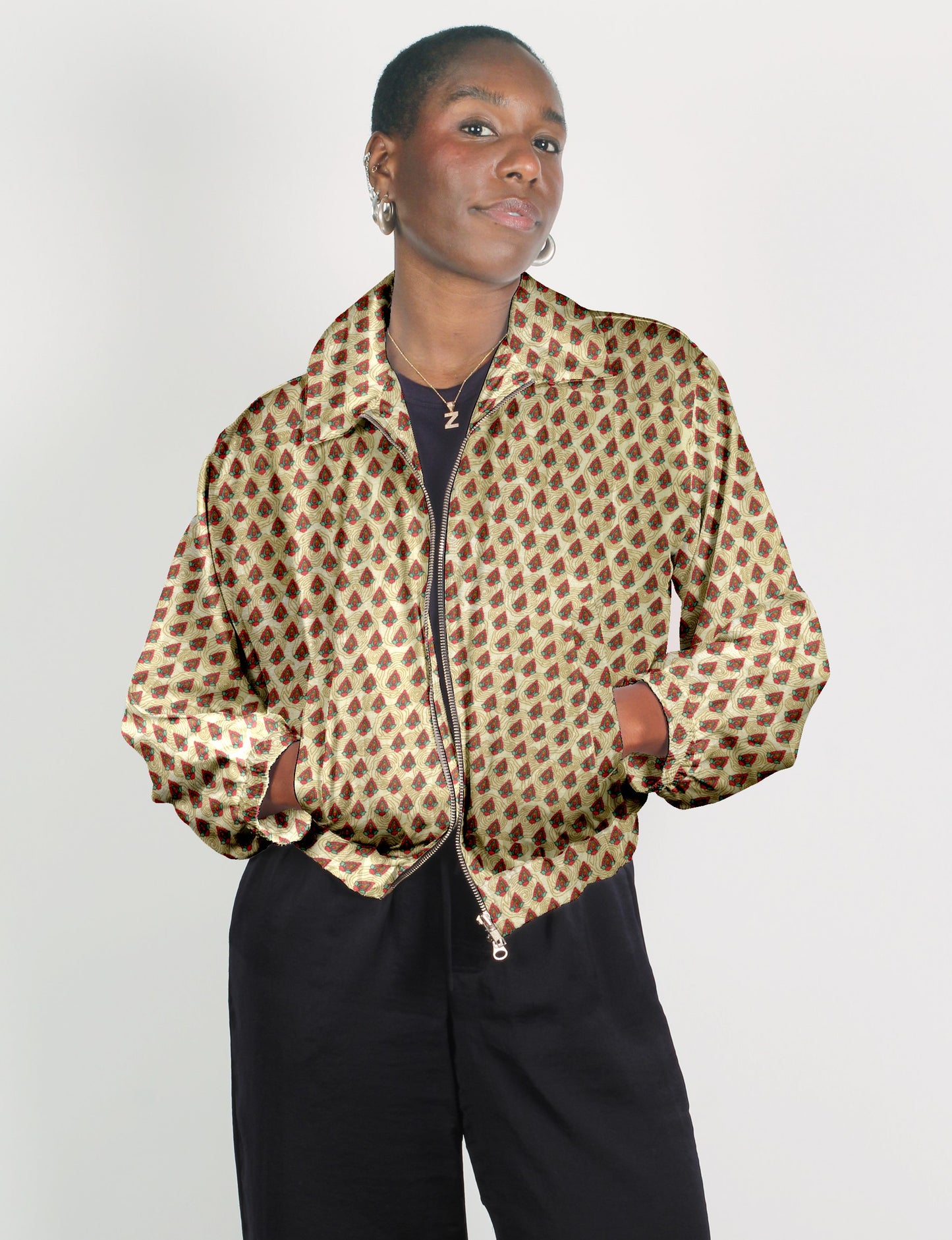 Woman wearing beige bomber jacket with red and green Indian ethnic pattern, front zipper, and elastic cuffs, paired with