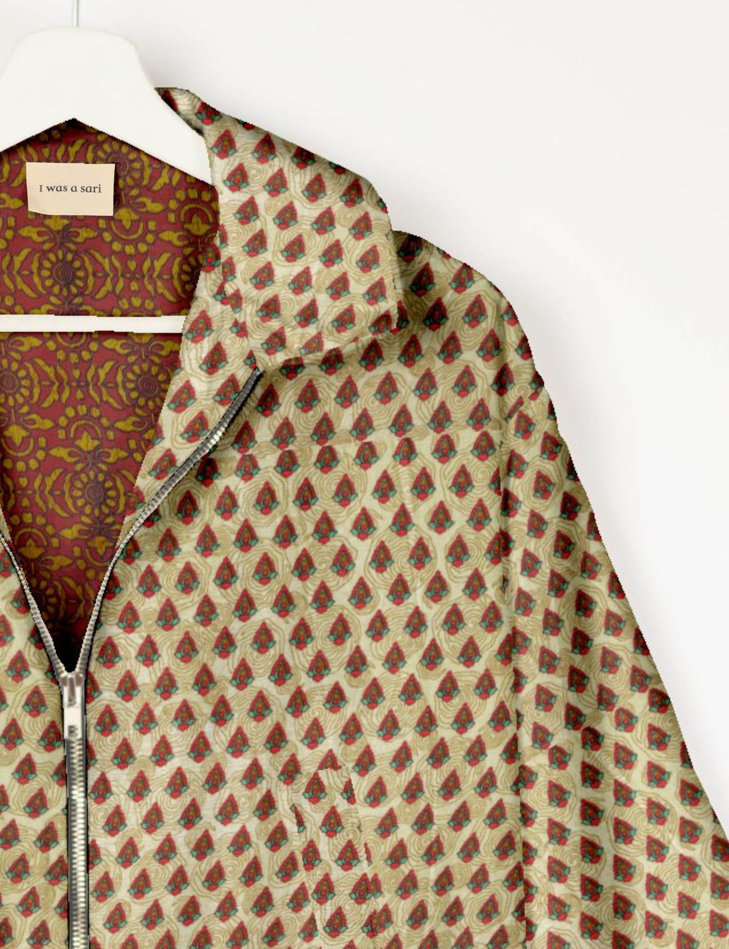 Beige bomber jacket with red and green ethnic print, silver zipper, and maroon patterned inner lining on white hanger