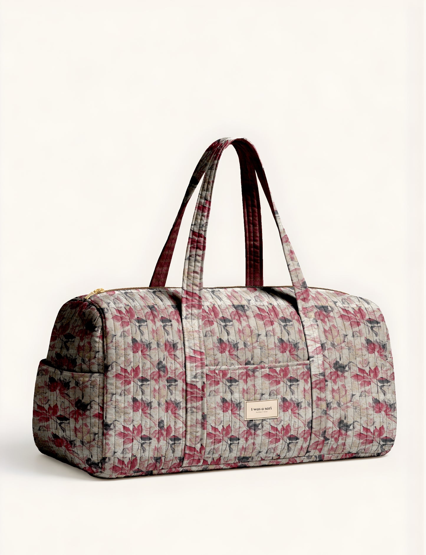 Quilted barrel bag with beige, red, and gray leaf pattern, dual handles, front pocket, and gold zipper closure