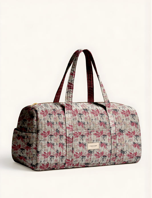 Quilted barrel bag with beige, red, and gray leaf pattern, dual handles, front pocket, and gold zipper closure