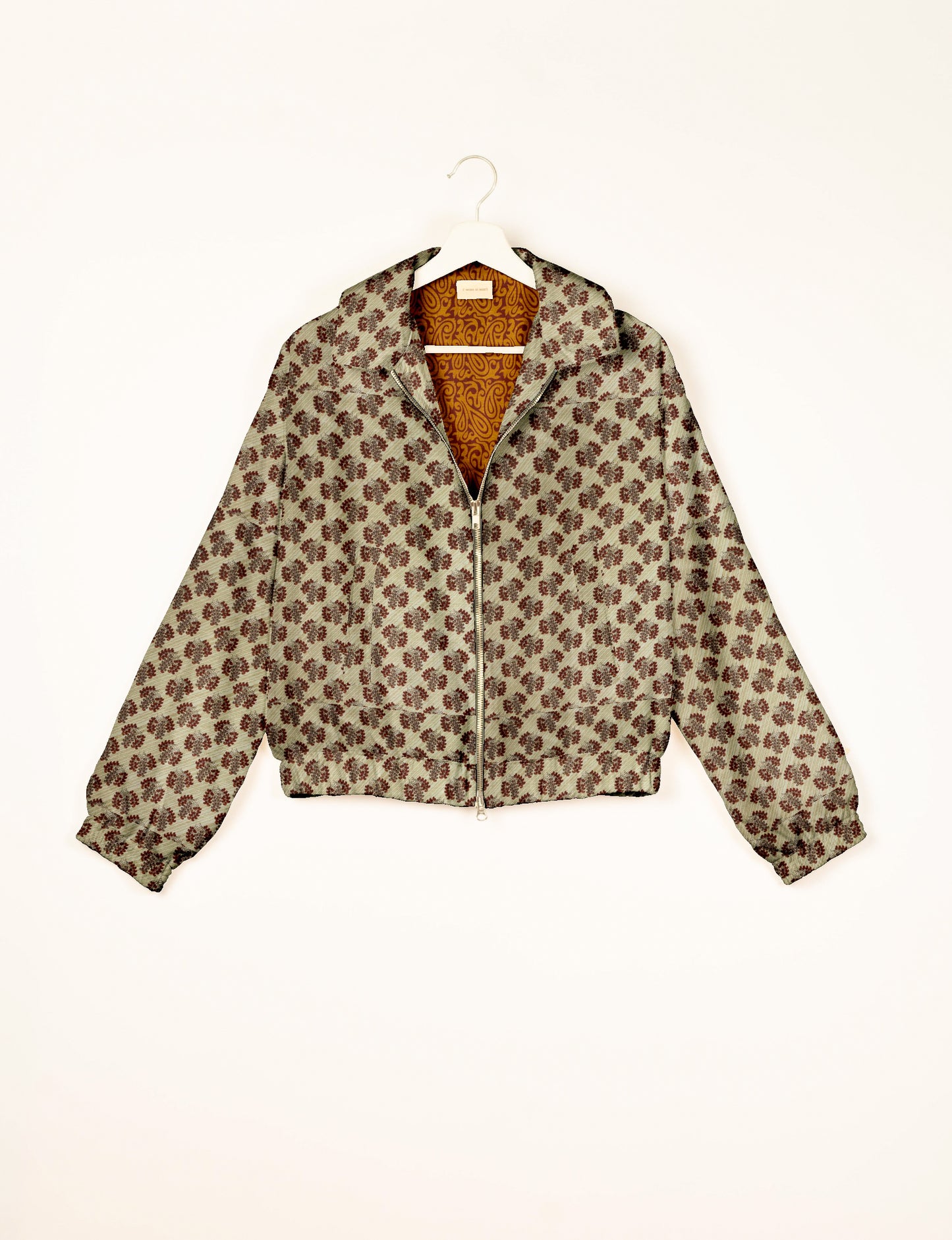 Beige bomber jacket with brown leaf pattern, front zipper, elastic cuffs and hem, shown hanging on white hanger