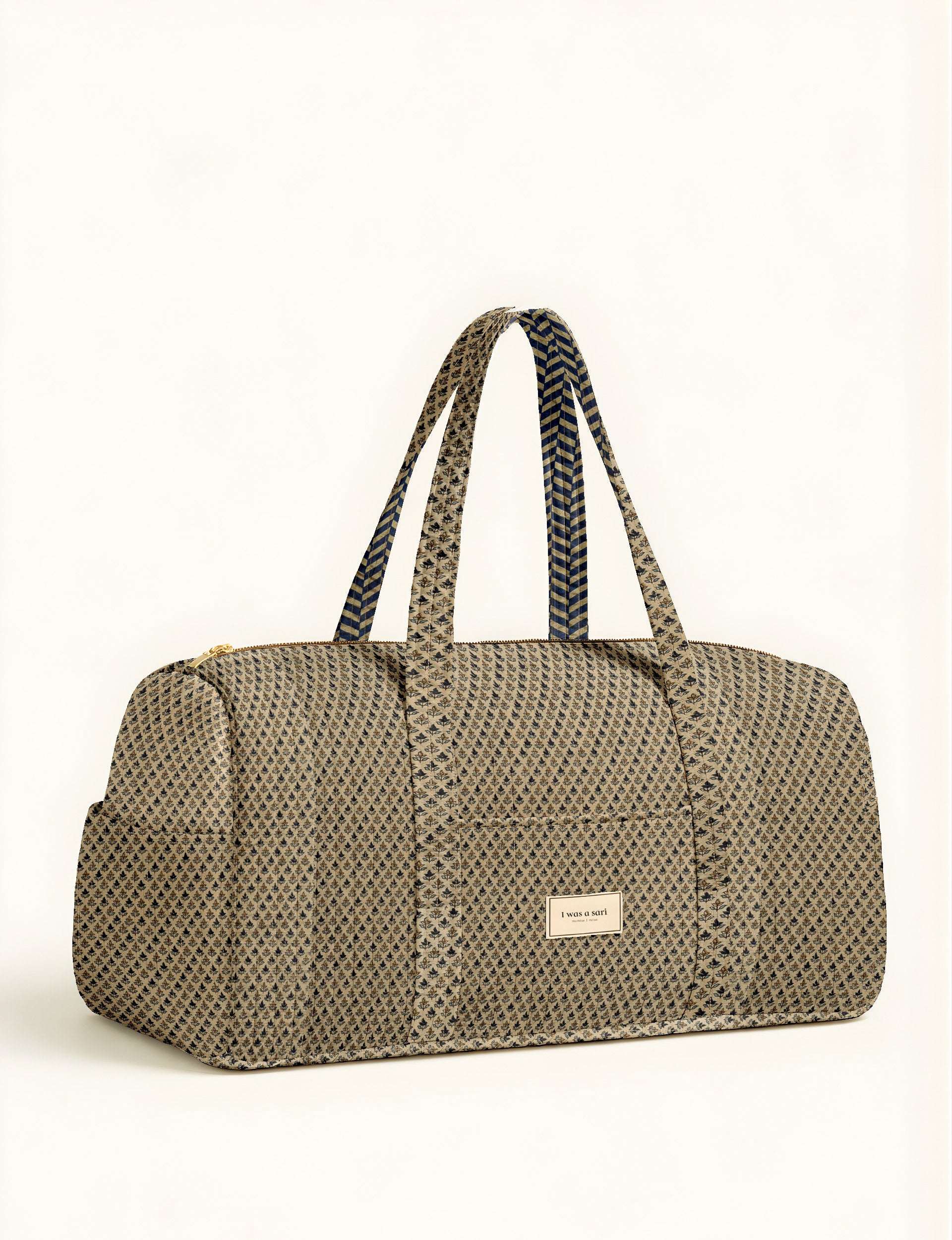 Beige quilted barrel bag with micro floral pattern, dual patterned handles, front pocket, and gold zipper, front view flat