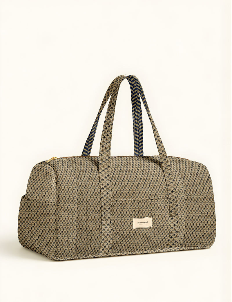 Beige quilted barrel bag with micro floral pattern, dual patterned handles, front pocket, and gold zipper, front view flat