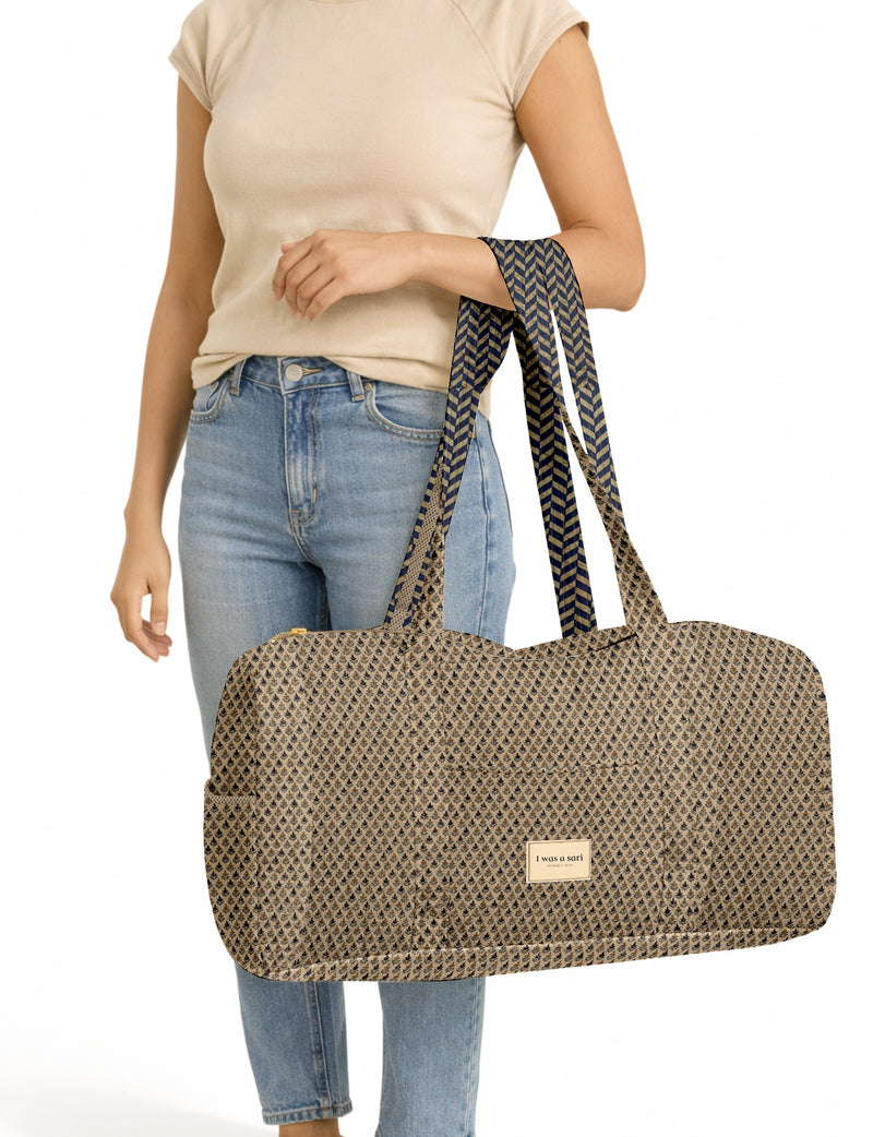 Woman wearing beige t-shirt and blue jeans holding a beige barrel bag with black micro print and navy chevron straps