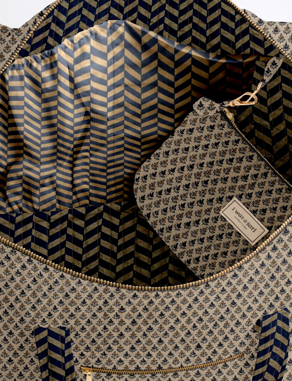 Beige quilted barrel bag with navy blue chevron and floral micro design, gold zipper, and fabric pouch inside with label