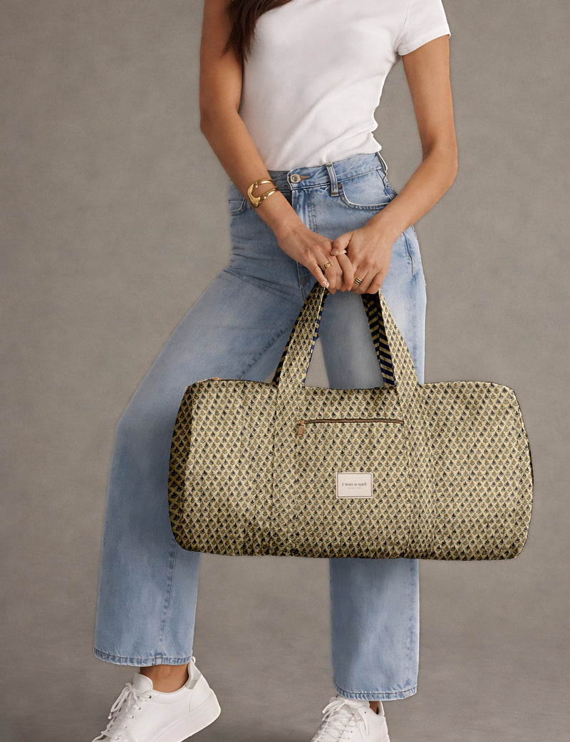 Woman wearing light blue jeans and white sneakers holding a beige quilted bowling bag with micro floral design and front