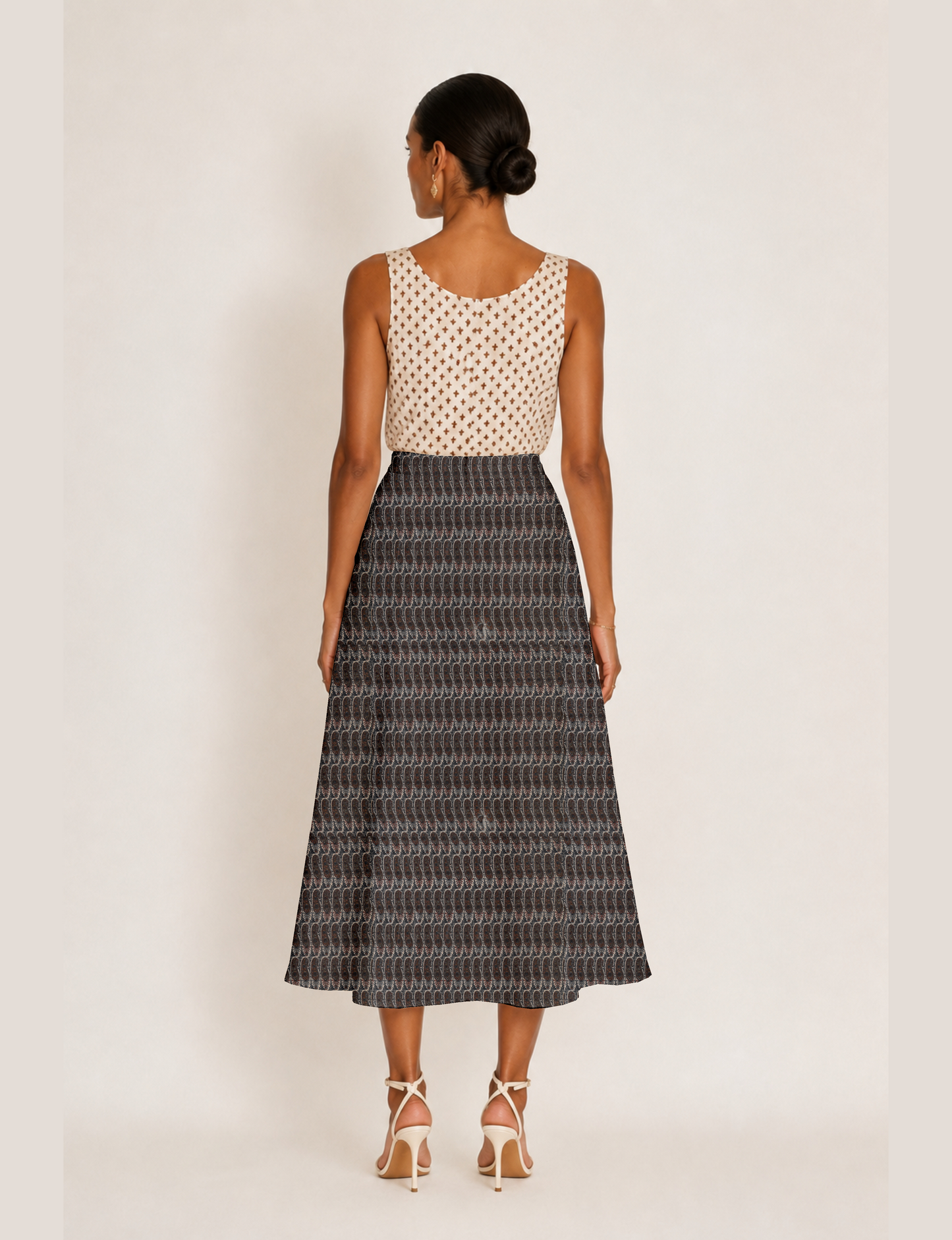 Woman wearing a yellow and black micro patterned A-line skirt with front slit, paired with beige sleeveless top and black