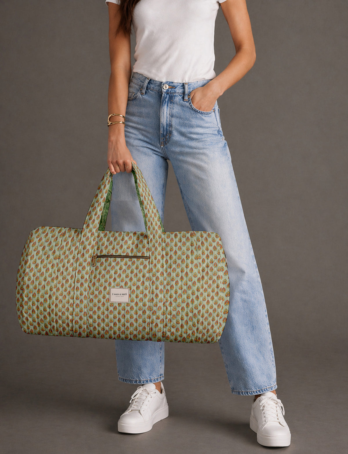 Quilted brown paisley barrel bag with double handles, front pocket, and gold zipper, shown in side angle view