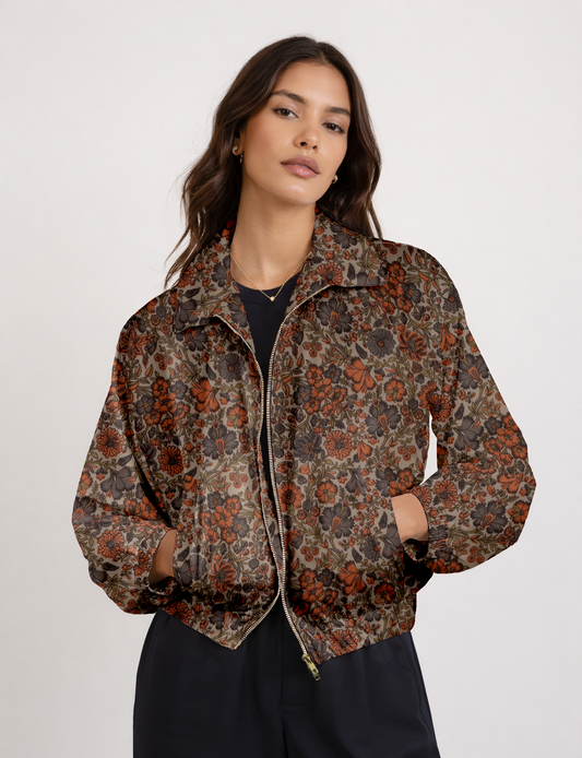 Woman wearing beige bomber jacket with tropical floral print in orange and gray, front view, zipped and hands in pockets