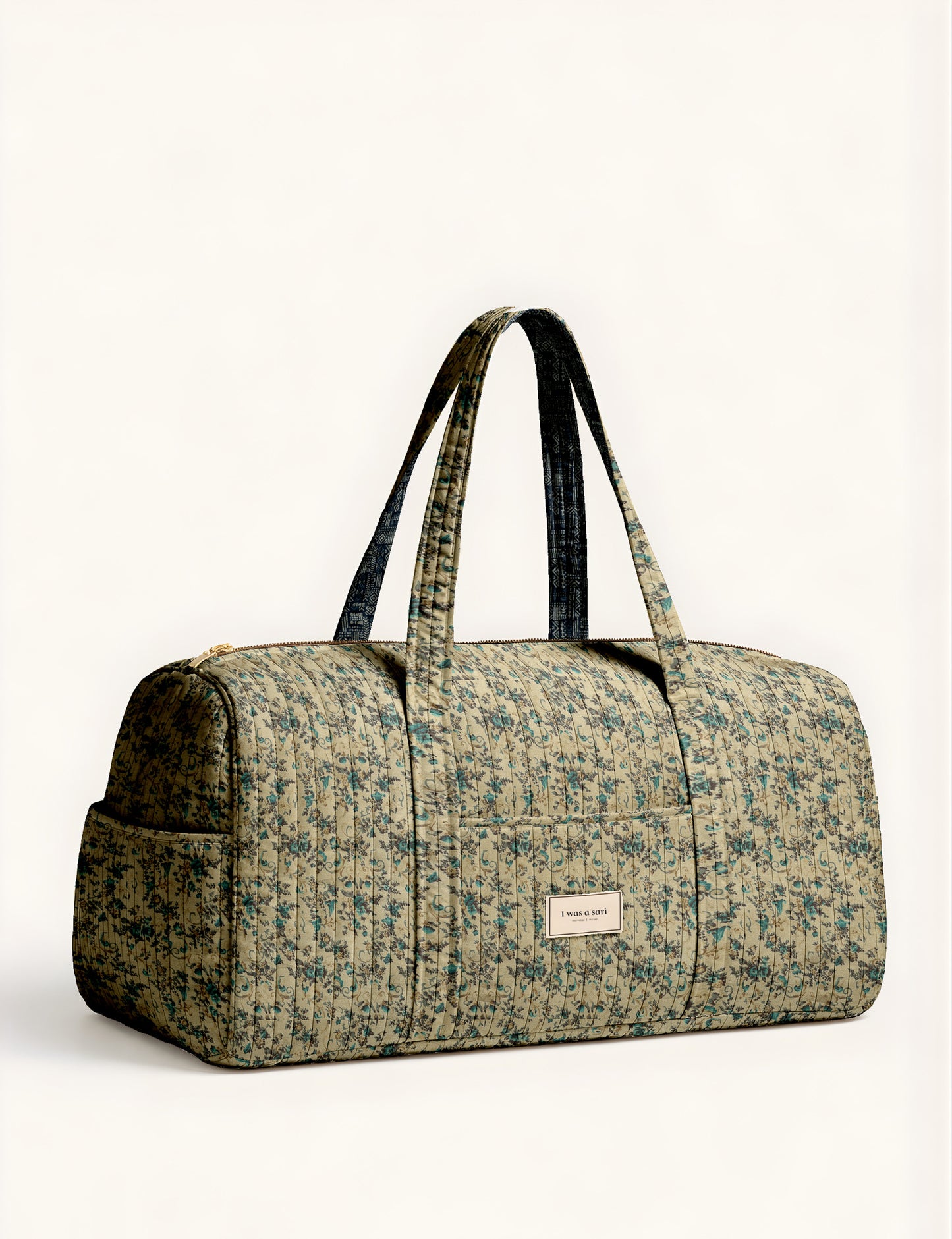 Woman holding a brown paisley quilted barrel bag with front zipper pocket, wearing light blue jeans and white sneakers
