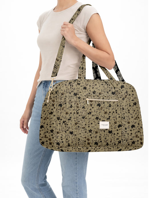 Brown quilted duffle bag with paisley pattern, front zip pocket, dual handles, and label reading "I was a sari"