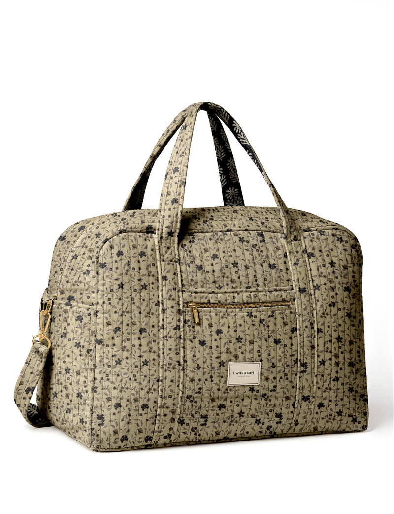 Brown quilted duffle bag with paisley pattern, front zip pocket, dual handles, and label reading "I was a sari"