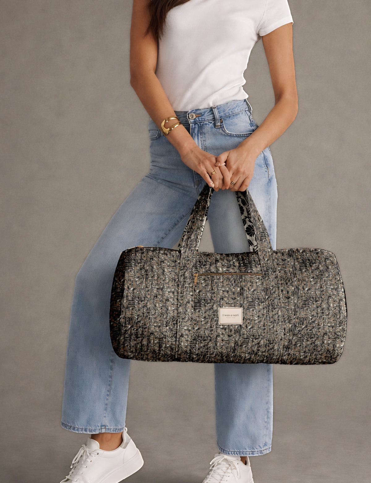 Quilted black abstract bowling bag with front zipper pocket, held by person wearing white top and light blue jeans