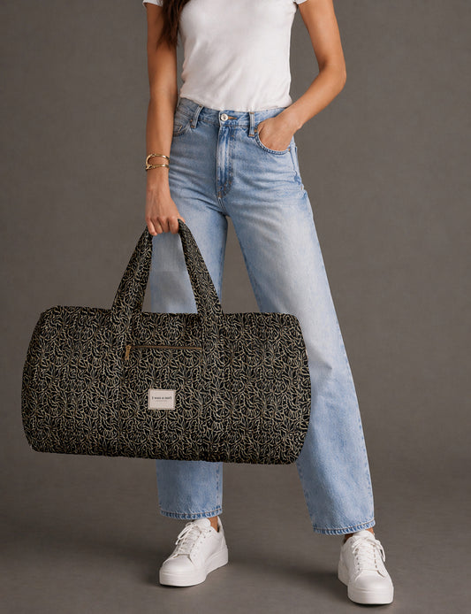 Quilted brown paisley barrel bag with double handles, front pocket, and gold zipper, shown in side angle view