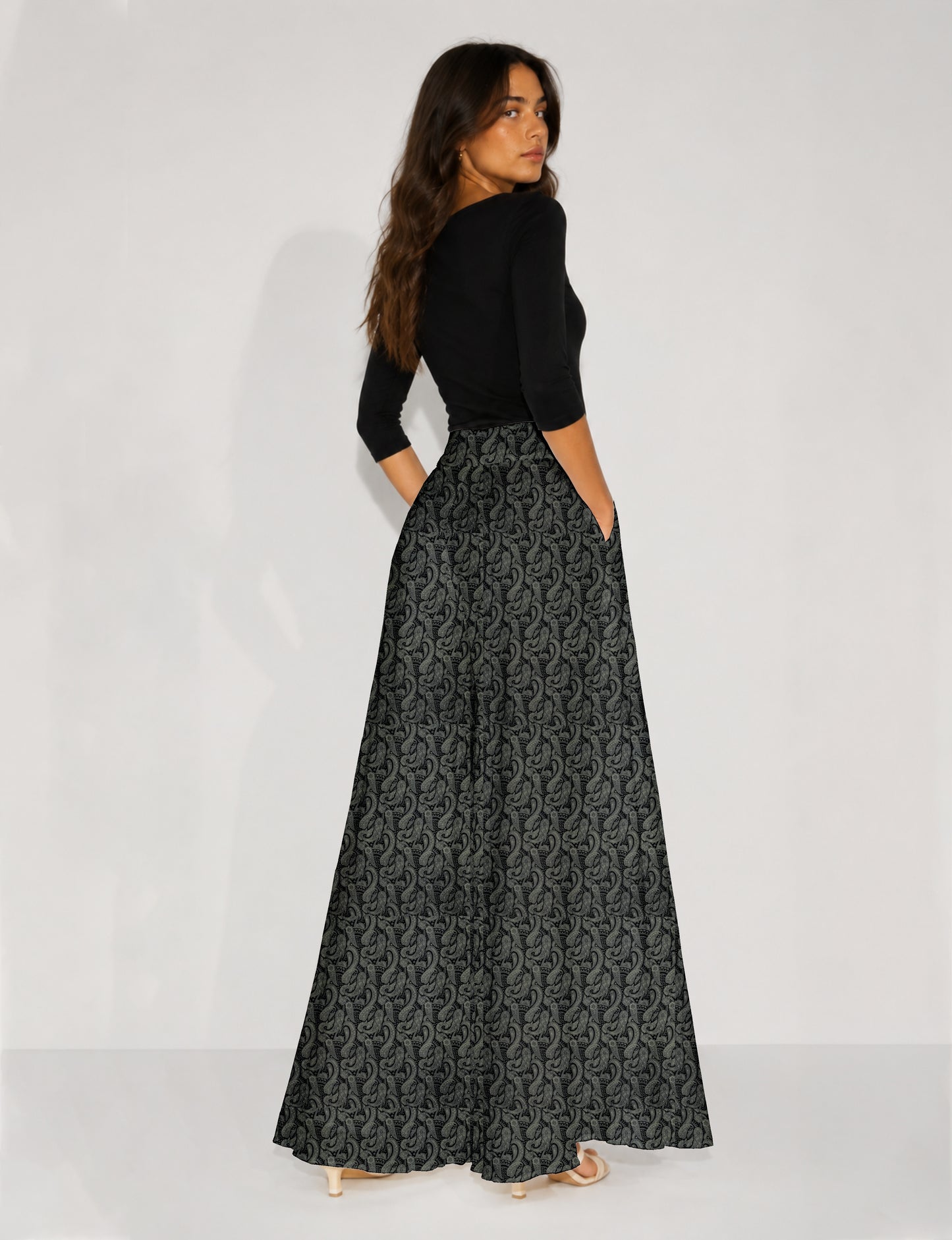 Woman wearing blue wide leg palazzo trousers with black and brown tropical floral print, side pockets, shown from back angle