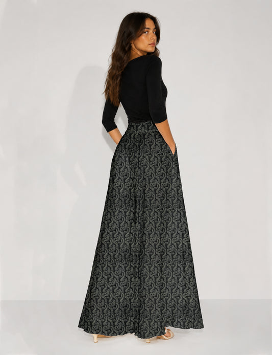 Woman wearing blue wide leg palazzo trousers with black and brown tropical floral print, side pockets, shown from back angle