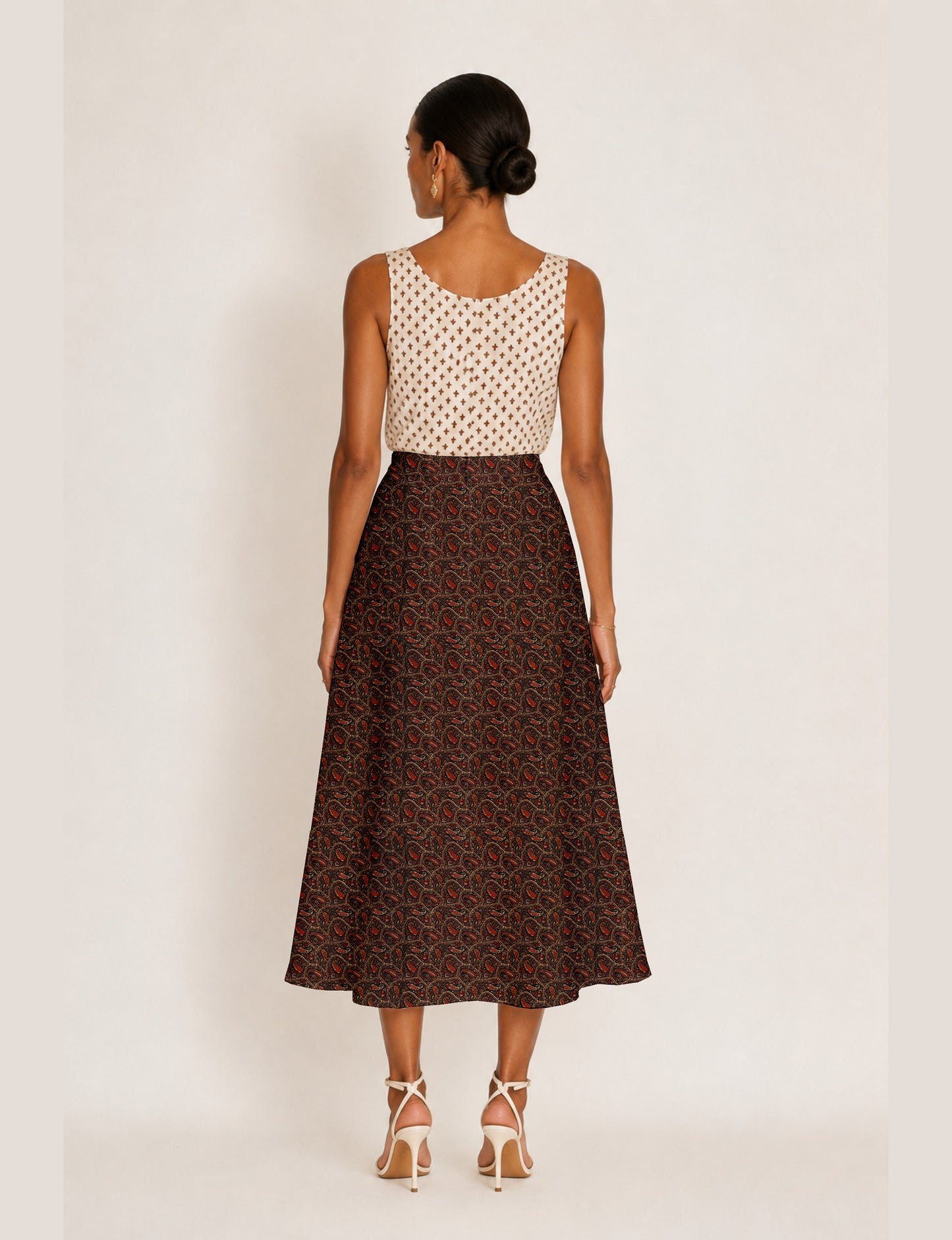 Woman wearing a yellow and black micro patterned A-line skirt with front slit, paired with beige sleeveless top and black