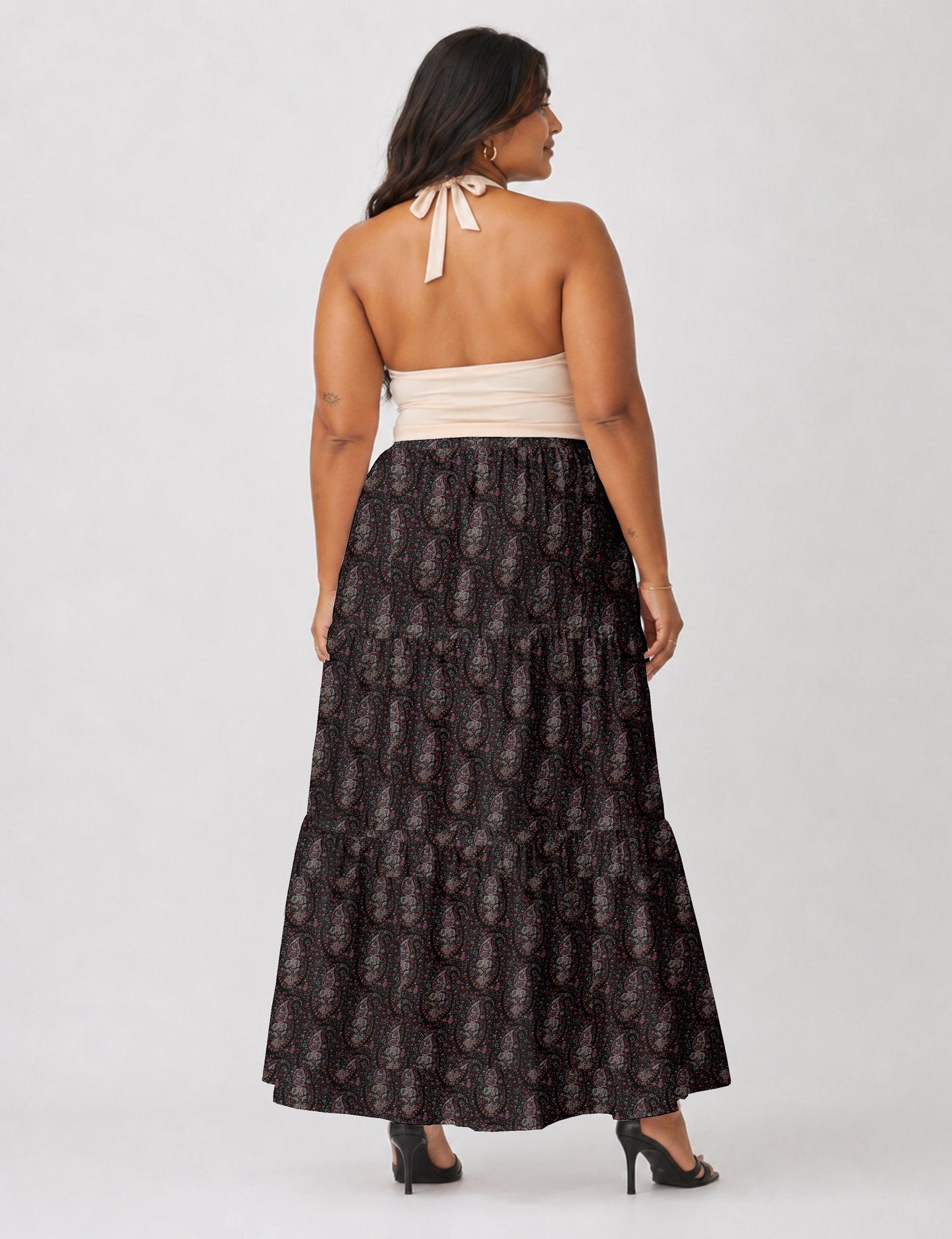 Woman wearing a yellow midi tiered skirt with a small geometric pattern, shown from the back, paired with beige top and