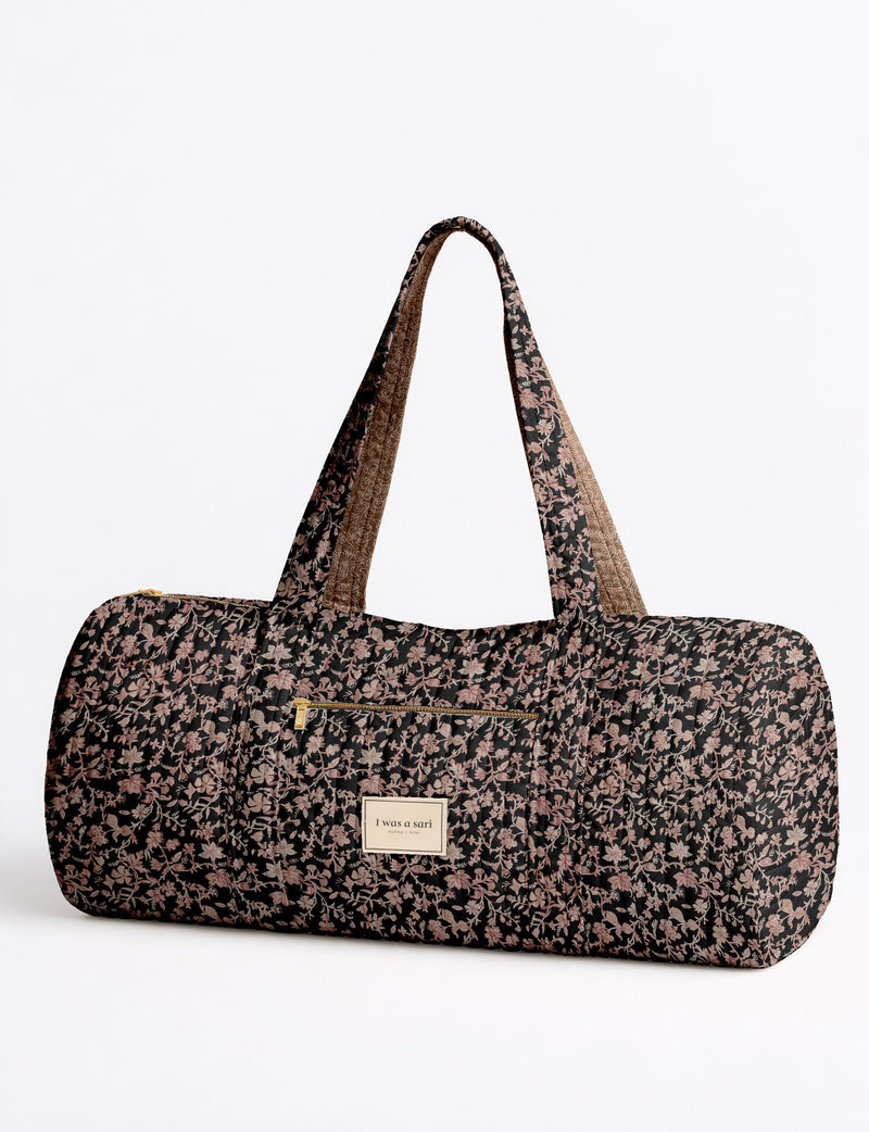 Brown paisley quilted bowling bag with front zipper pocket, held by person wearing white shirt and light blue jeans
