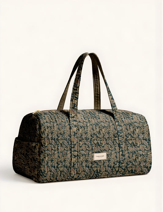 Quilted brown paisley barrel bag with double handles, front pocket, and gold zipper, shown in side angle view