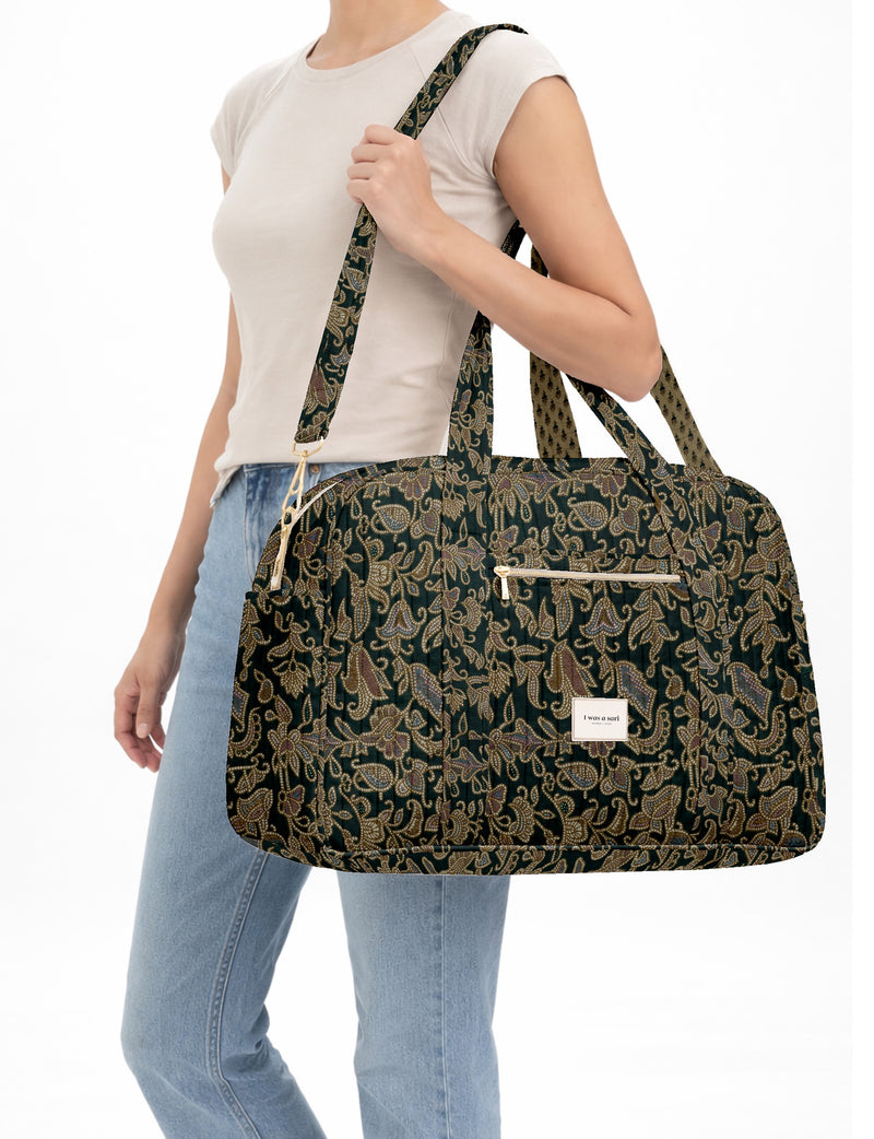 Brown quilted duffle bag with paisley pattern, front zip pocket, dual handles, and label reading "I was a sari"