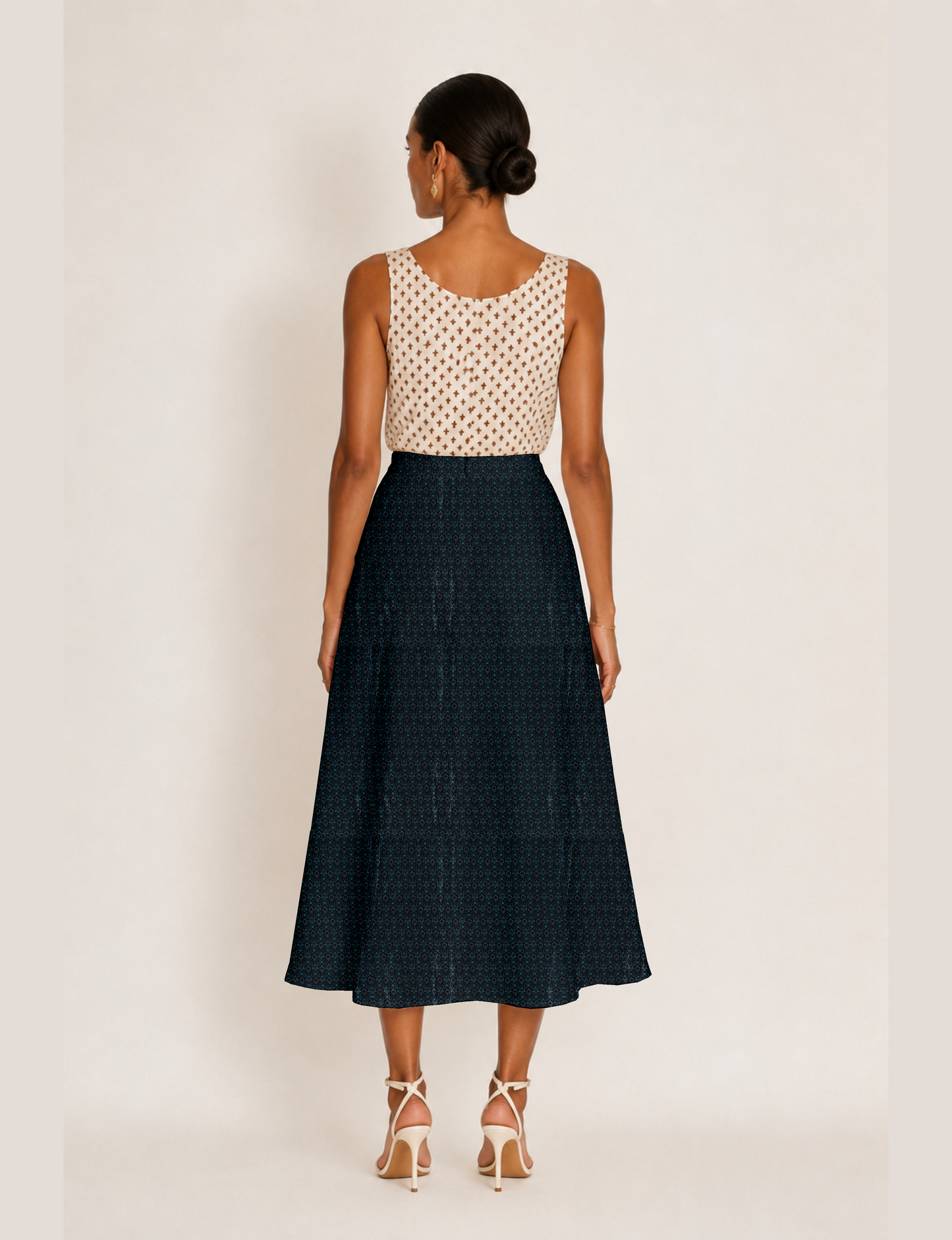 Woman wearing a yellow and black micro patterned A-line skirt with front slit, paired with beige sleeveless top and black