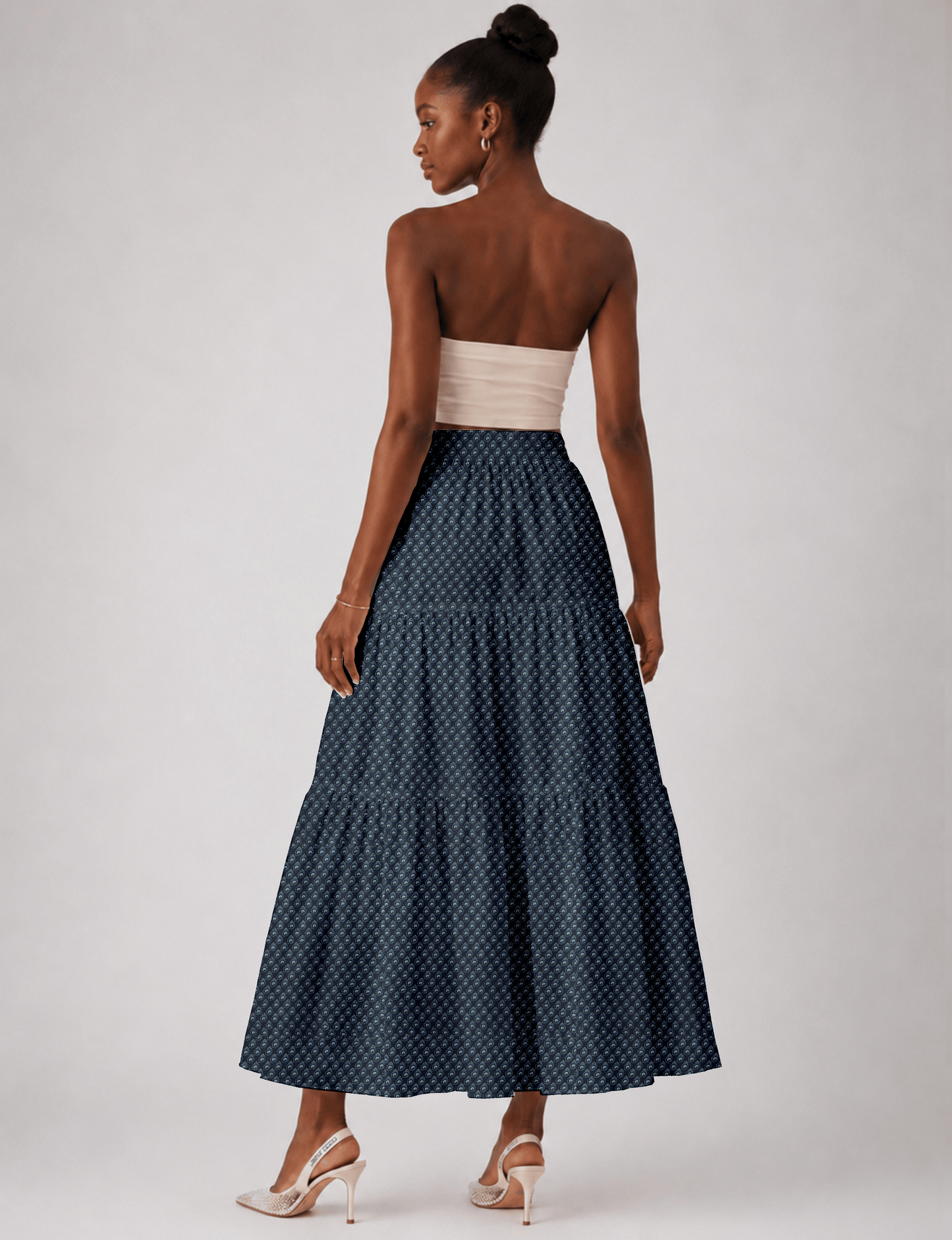 Woman wearing a yellow midi tiered skirt with a small geometric pattern, shown from the back, paired with beige top and
