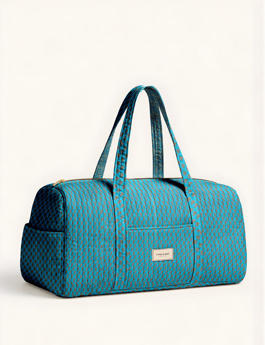 Quilted brown paisley barrel bag with double handles, front pocket, and gold zipper, shown in side angle view