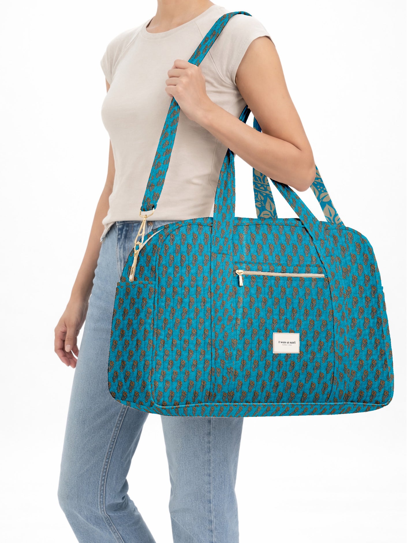 Brown quilted duffle bag with paisley pattern, front zip pocket, dual handles, and label reading "I was a sari"
