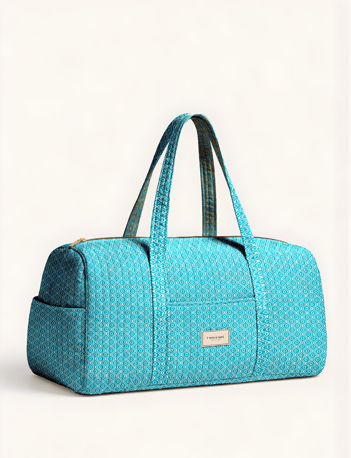 Quilted brown paisley barrel bag with double handles, front pocket, and gold zipper, shown in side angle view