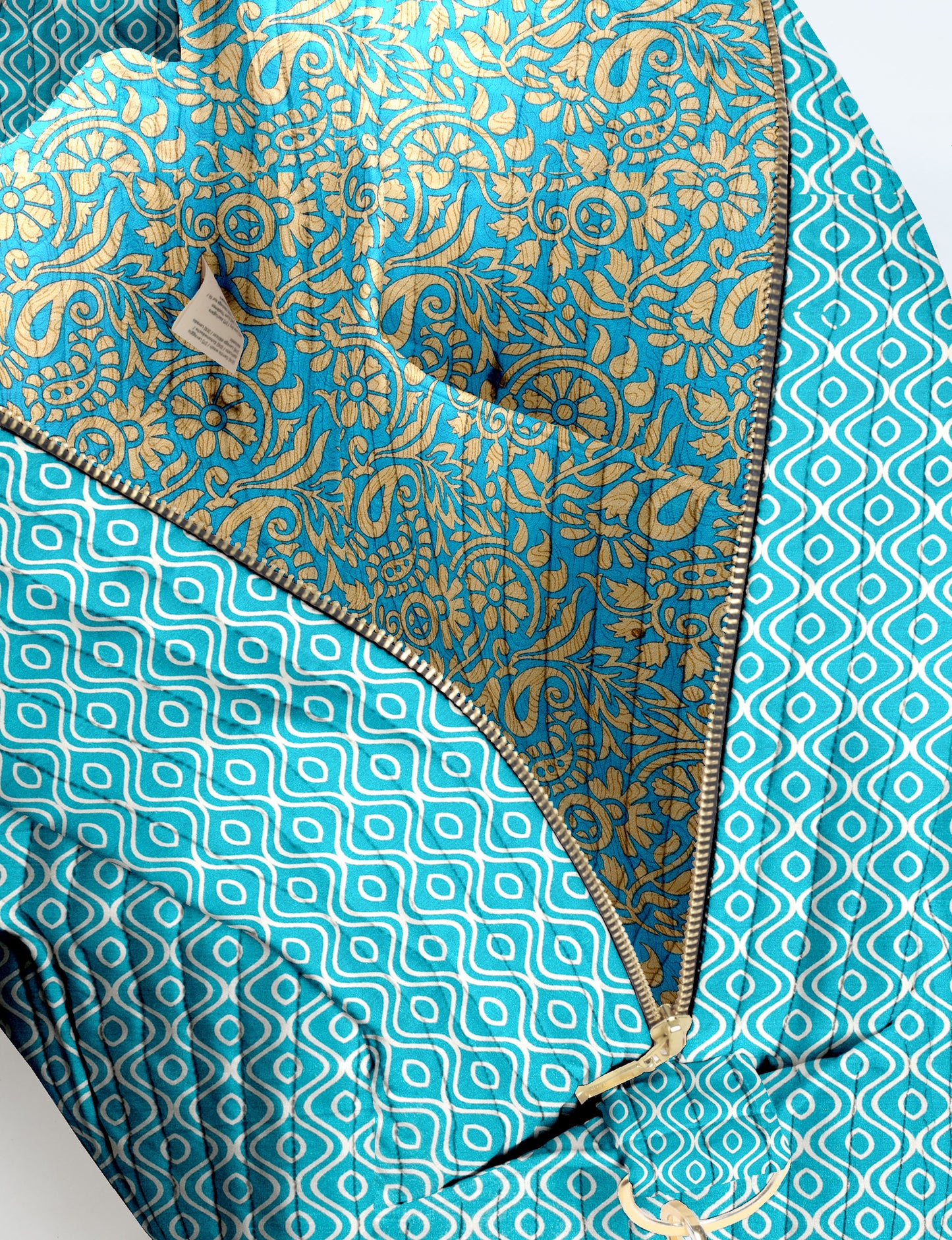 Brown quilted duffle bag with paisley pattern, front zip pocket, dual handles, and label reading "I was a sari"