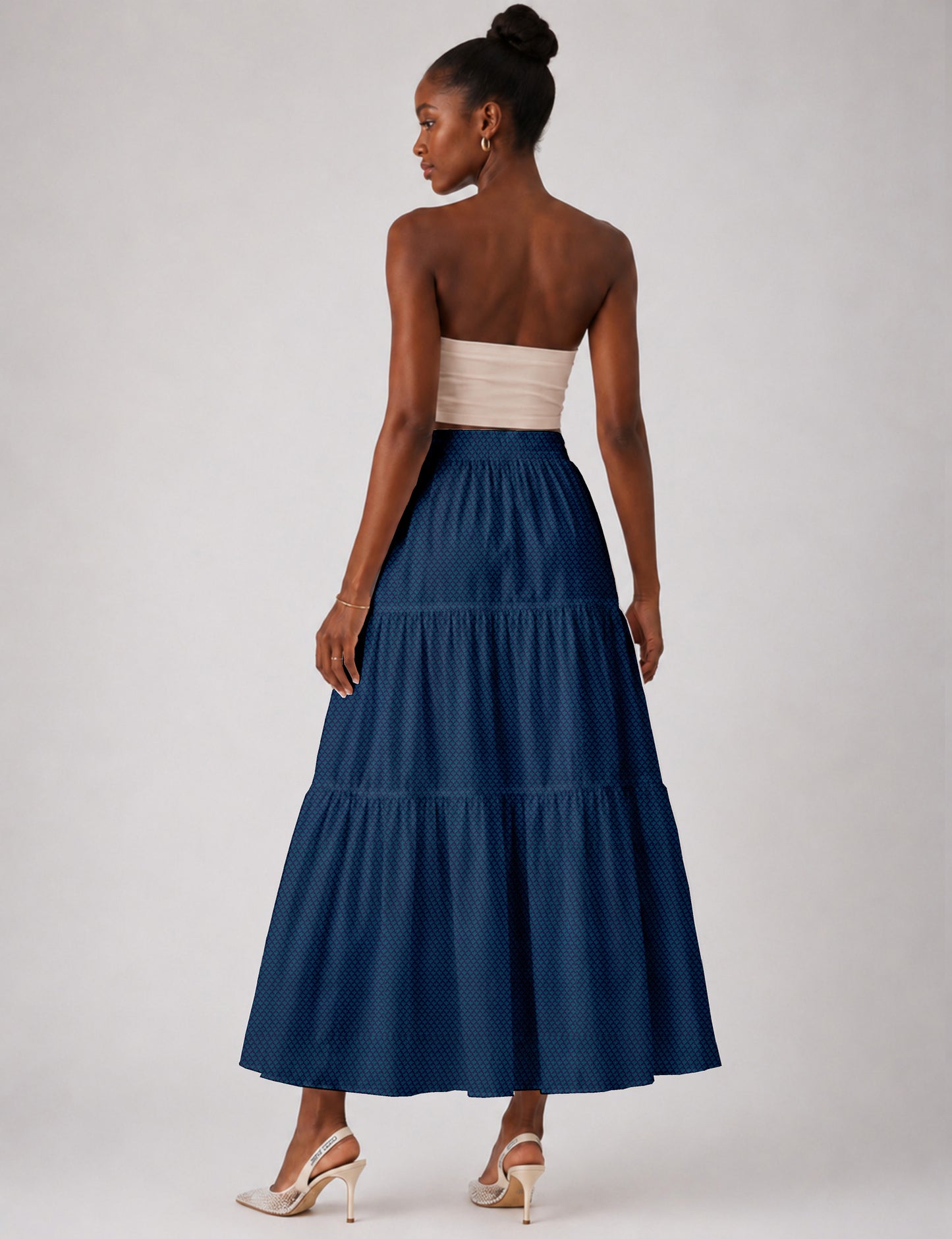 Woman wearing a yellow midi tiered skirt with a small geometric pattern, paired with a beige strapless top and white heels