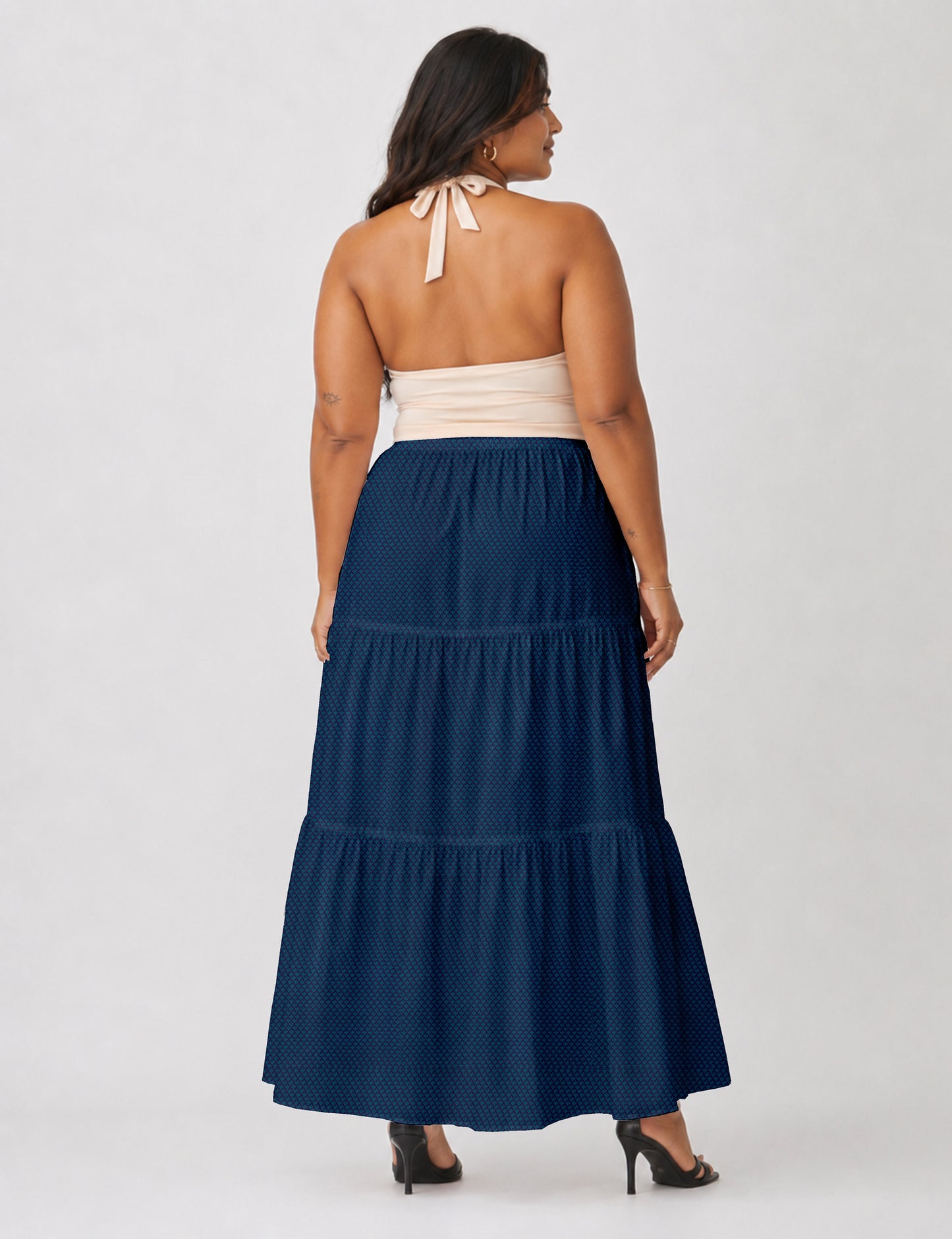 Woman wearing a yellow midi tiered skirt with a small geometric pattern, shown from the back, paired with beige top and