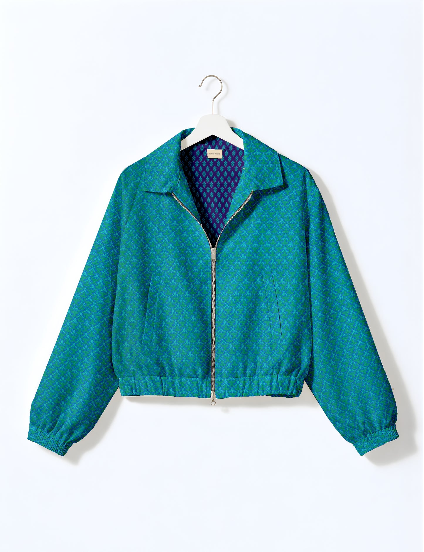 Blue bomber jacket with green micro pattern, front zipper, elastic cuffs and waistband, hanging on white hanger