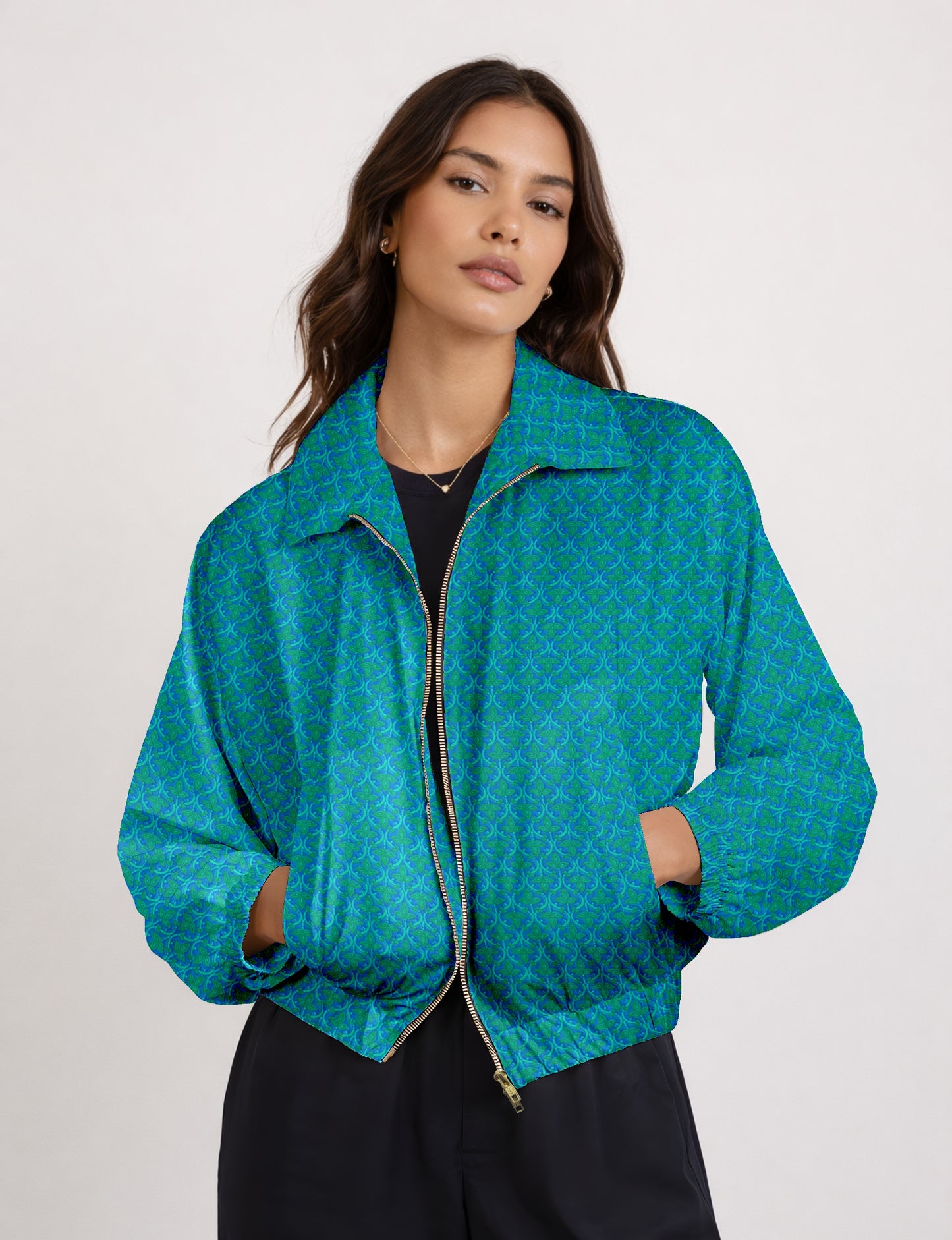 Woman wearing a blue bomber jacket with a green micro pattern, front zipper, and elastic cuffs, paired with black pants