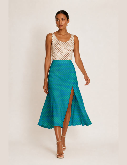 Woman wearing a blue A-line skirt with micro pattern and front slit, paired with a sleeveless beige top with brown cross