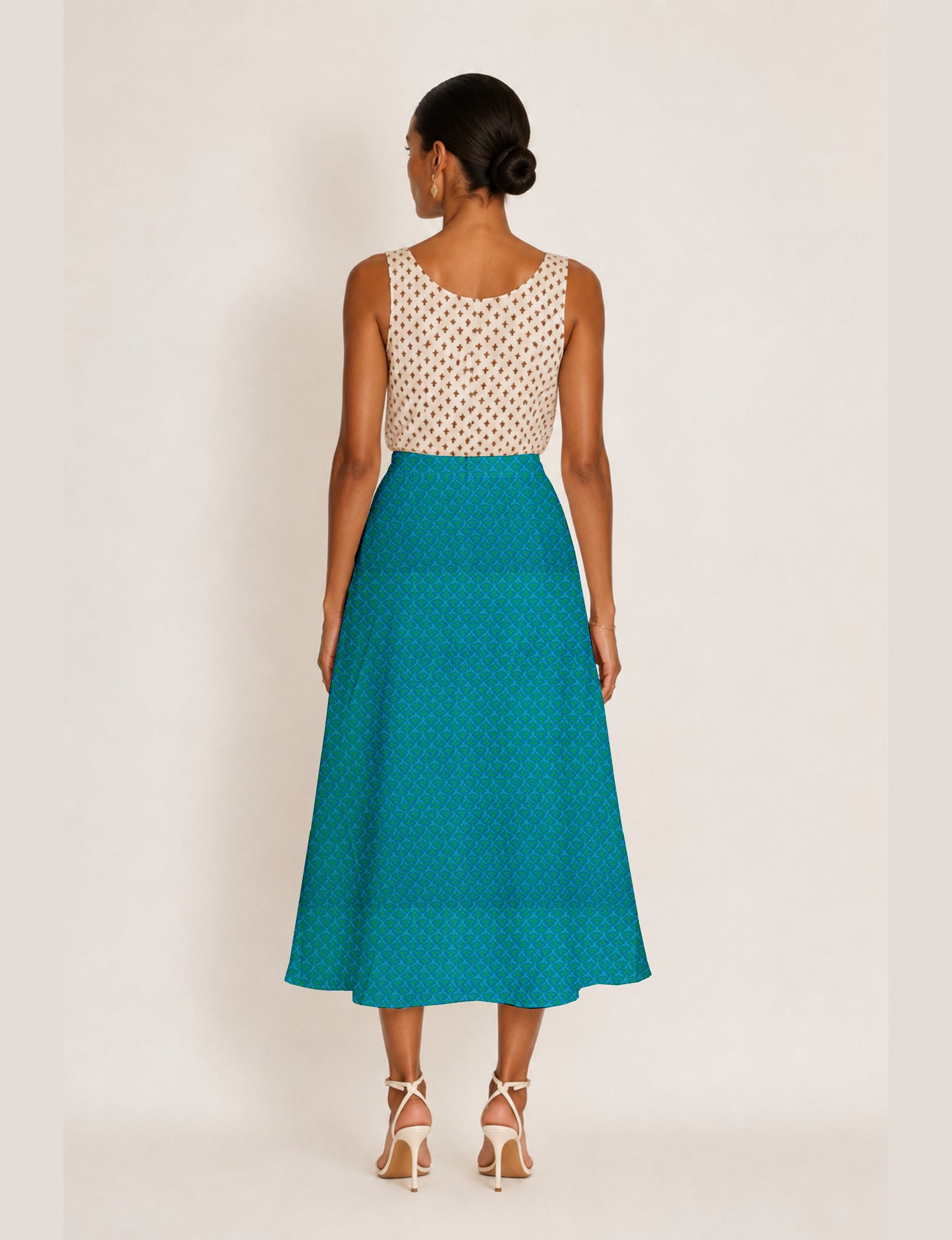 Woman wearing a blue A-line skirt with micro pattern and slit, shown from back, paired with sleeveless beige top with brown
