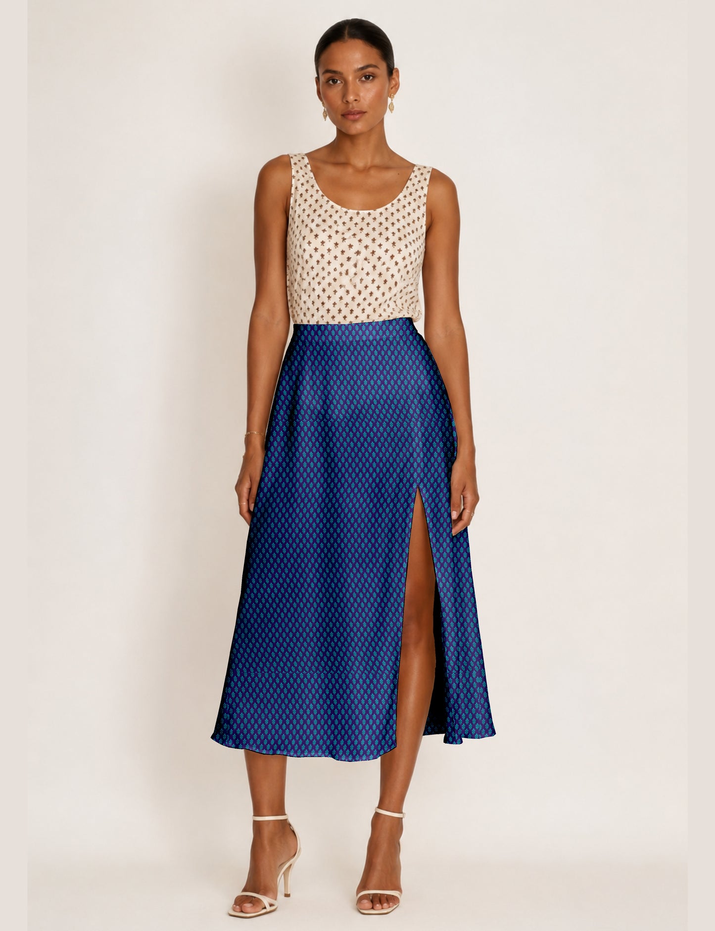 Woman wearing a blue A-line skirt with a micro pattern and front slit, paired with a sleeveless beige top with brown print