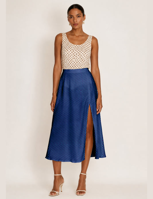 Woman wearing a blue A-line skirt with a micro pattern and front slit, paired with a sleeveless beige top with brown print