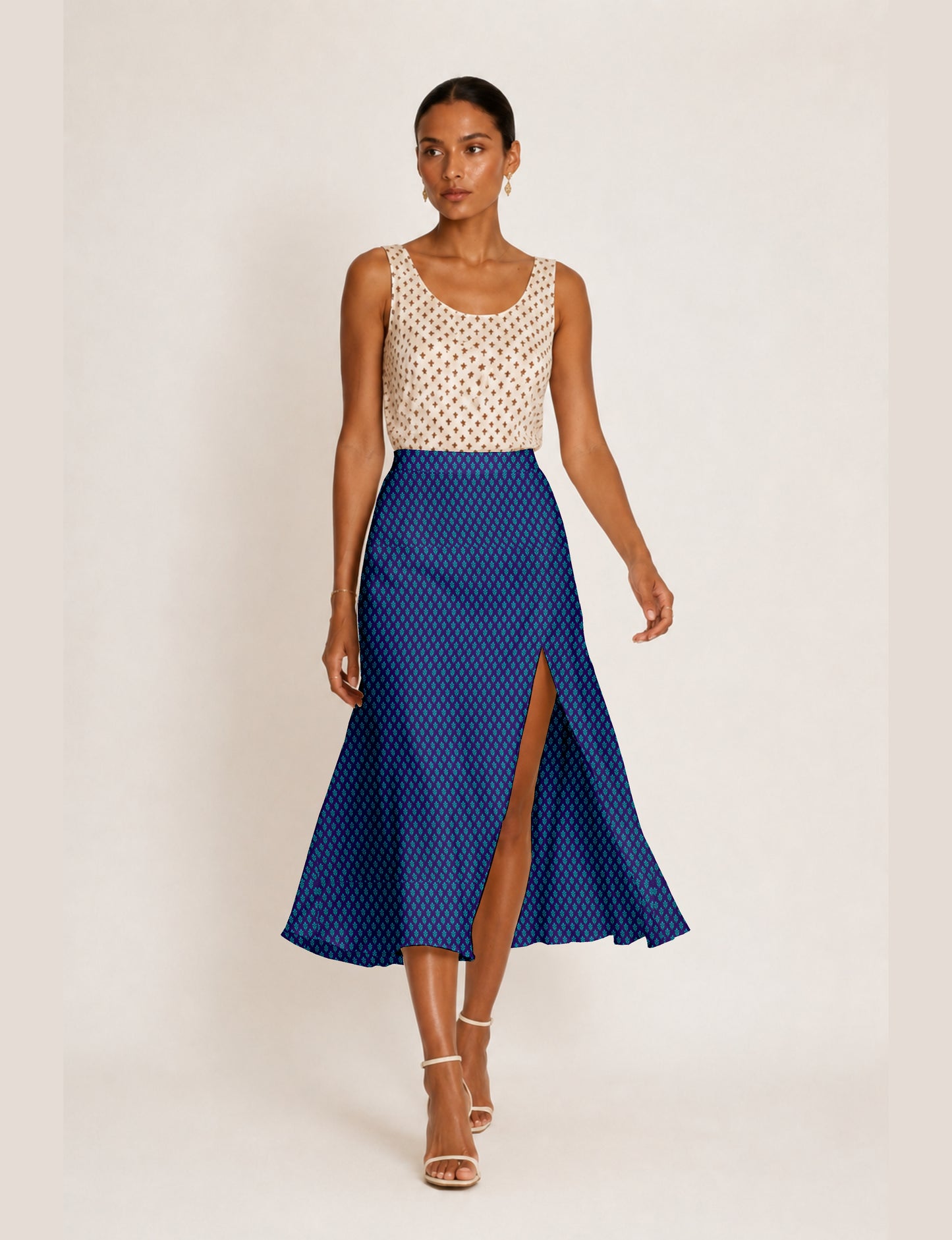 Woman wearing a blue A-line skirt with a small geometric pattern and front slit, paired with a sleeveless beige top with