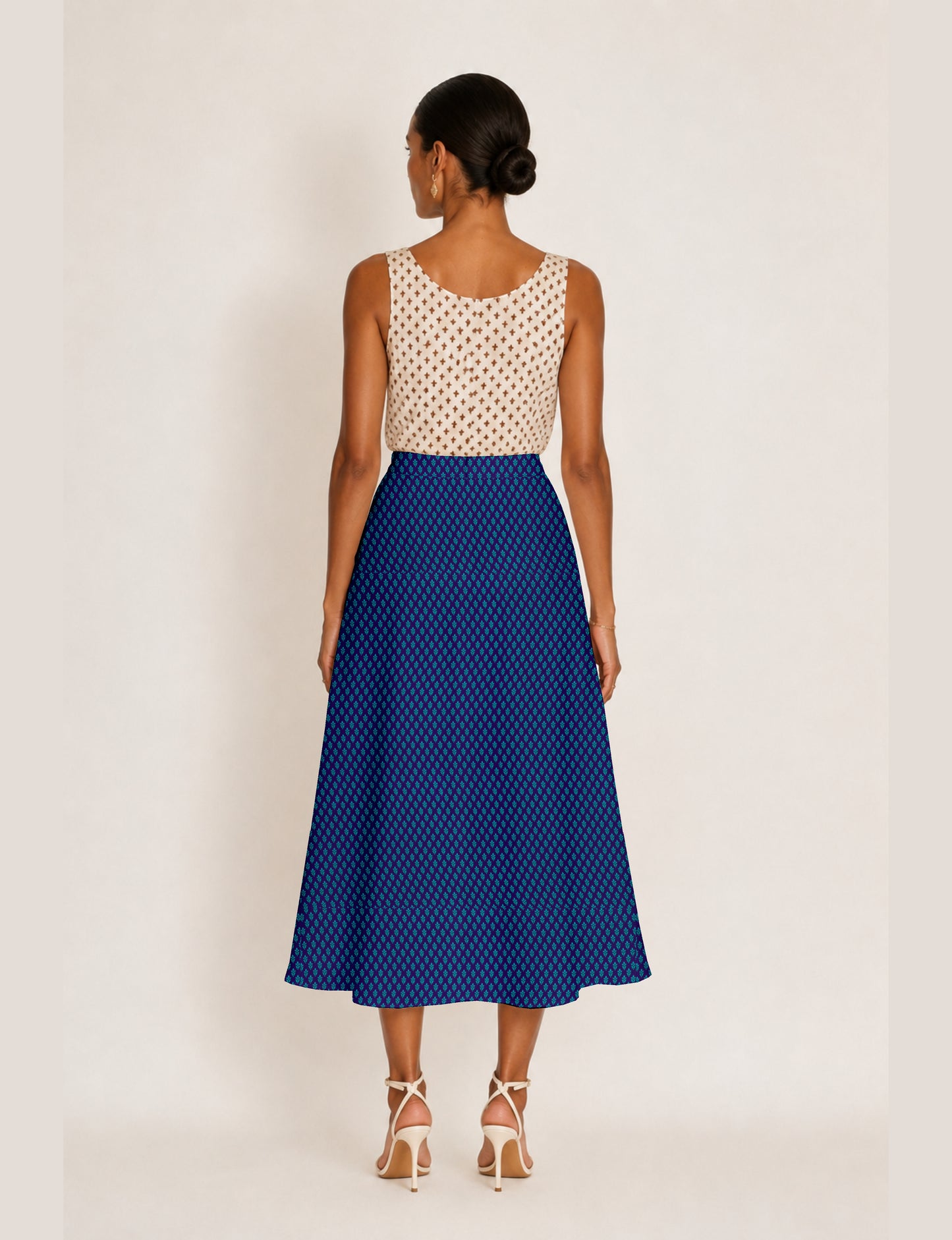 Woman wearing a blue A-line skirt with a small geometric pattern, viewed from the back, paired with a sleeveless beige top