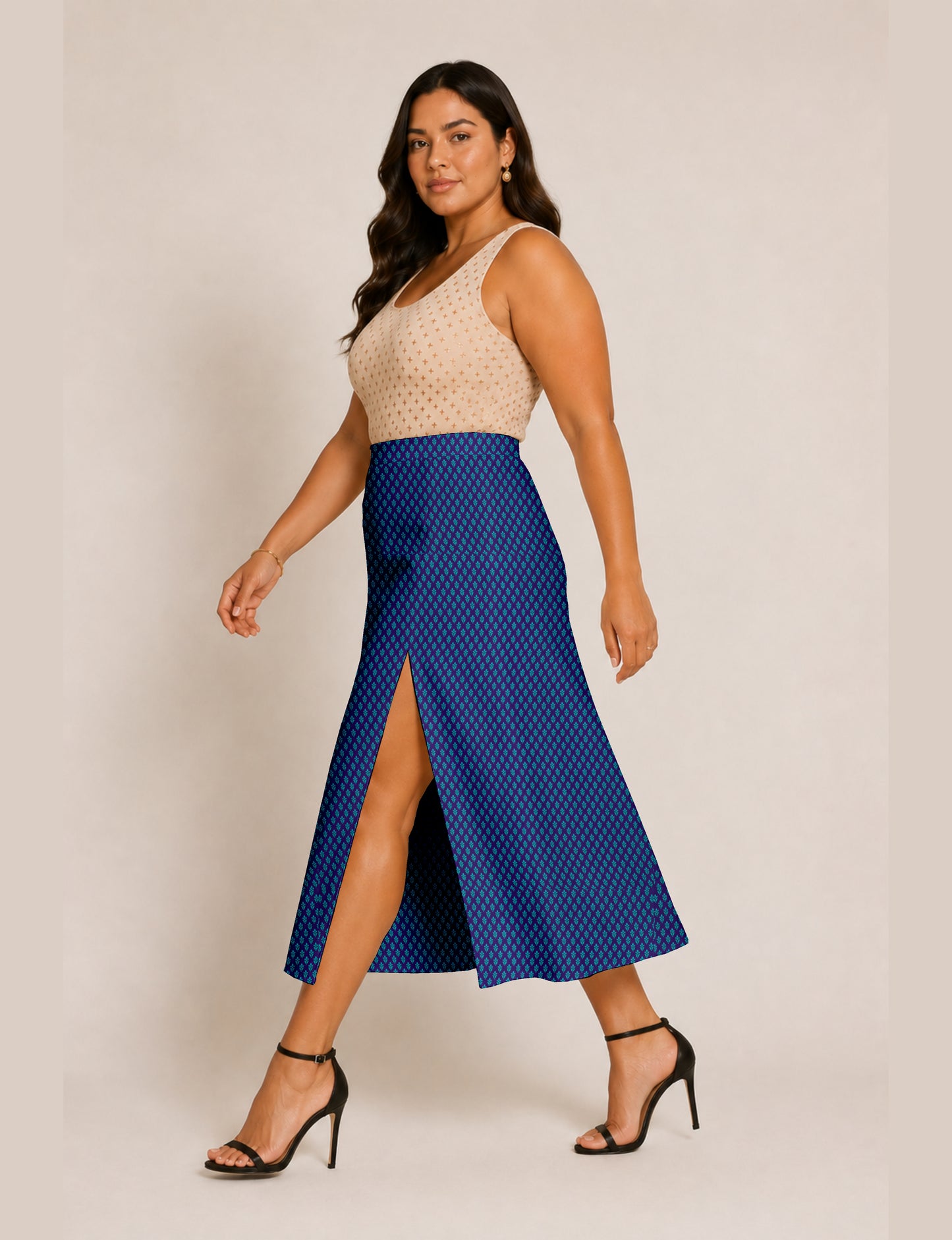 Woman wearing a blue A-line skirt with a micro pattern and front slit, paired with a beige sleeveless top and black heels
