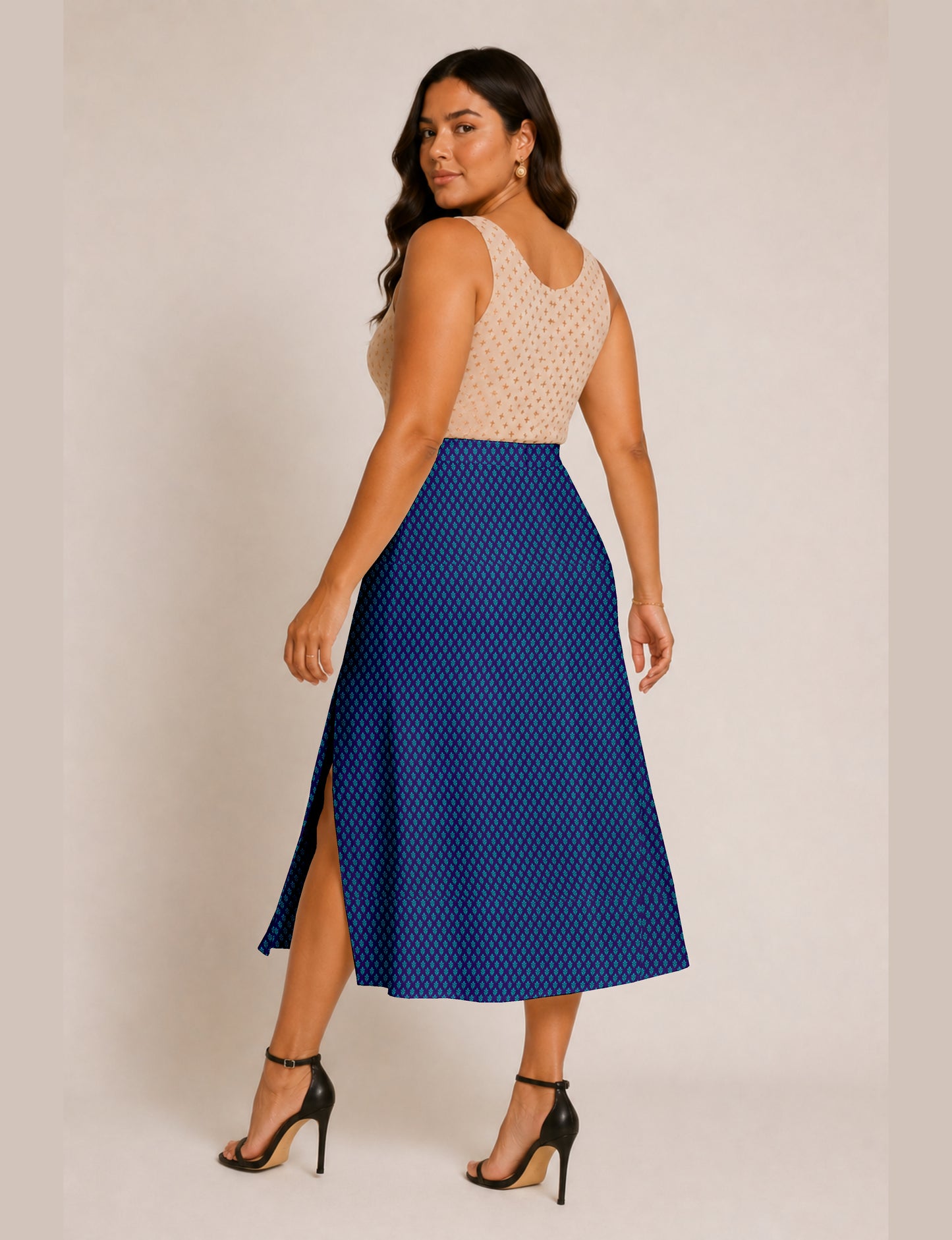 Woman wearing a blue A-line skirt with micro pattern and side slit, paired with a beige sleeveless top, back view